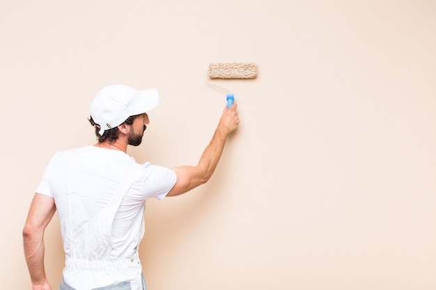 Young painter bearded man painting a wall with a paint roller