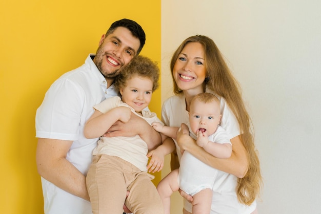 Young parents hold their sons' children in their arms Happy family on a white yellow background