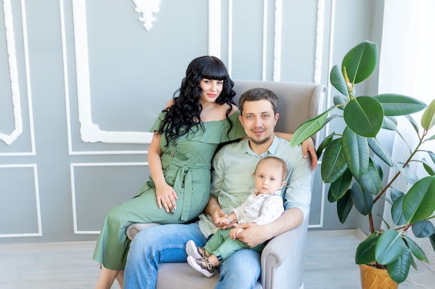 Young parents hug their baby in a bright room in green clothes, happy family concept, family Day