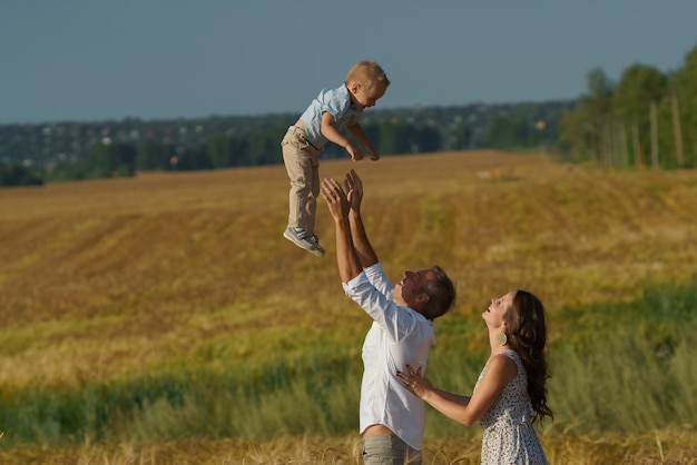 Young parents and kid walking through a wheat field. Mother, father and little boy leisures together outdoor. Family on summer meadow