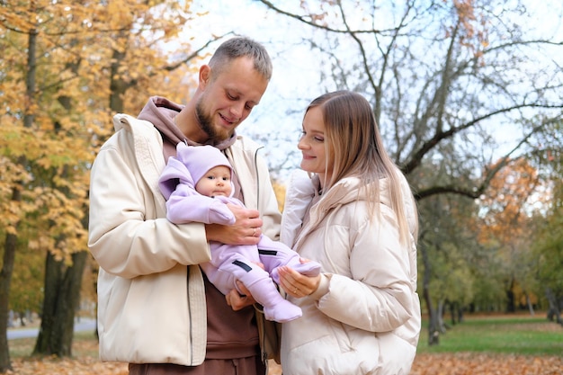 Young parents mother and father walk with a newborn baby in the autumn park