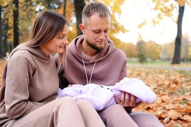 Young parents sit on a plaid with a newborn baby in an autumn park