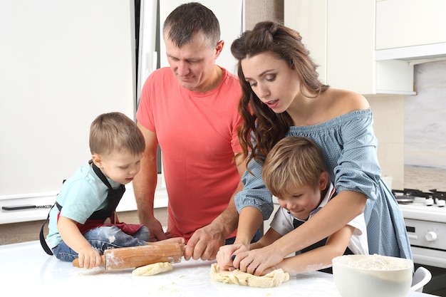 Young parents next to small children who knead the dough on the kitchen table