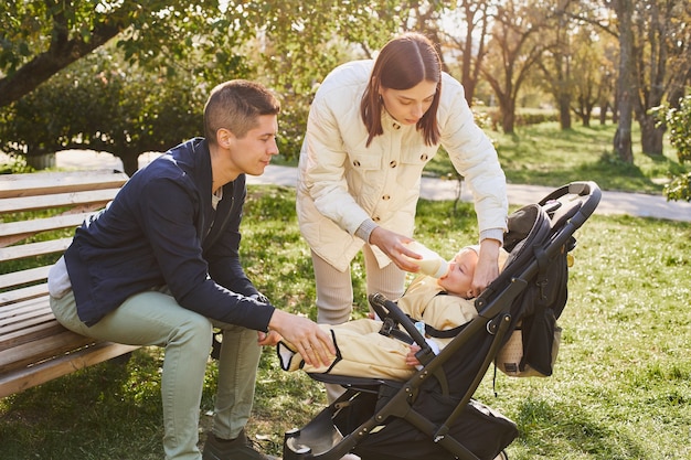 Young parents with a baby son in a stroller in the park.