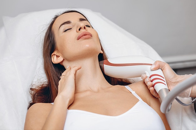 Young patient lies on a white couch and receives a cosmetic lifting procedure with a rejuvenation device in a beauty salon. Smoothing out wrinkles and getting younger. Aesthetic treatment of the skin.