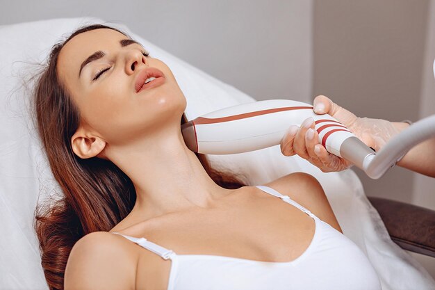 A young patient lies on a white couch and receives a cosmetic lifting procedure with a rejuvenation device in a beauty salon. Smoothing out wrinkles and getting younger.