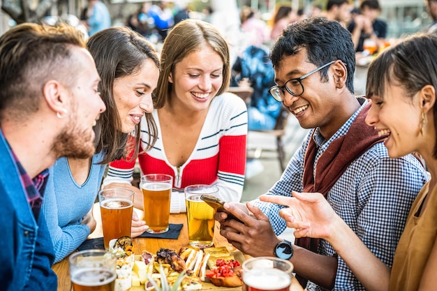 Young people having fun at beer pub millennials people drinking and eating at restaurant young students using smart devices for being active on social media