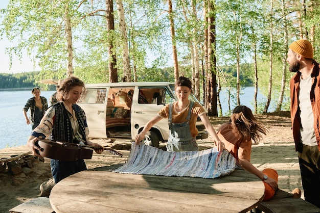 Young people setting the table they camping in the forest near the lake