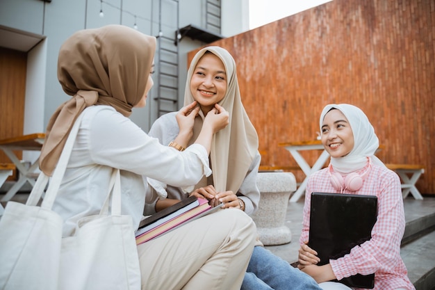 Young people sitting on stairs helping a friend wear hijab with buildings in the background