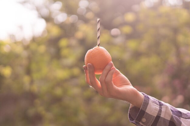 Young person holding and drinking the orange fruit with tubule inserted in it