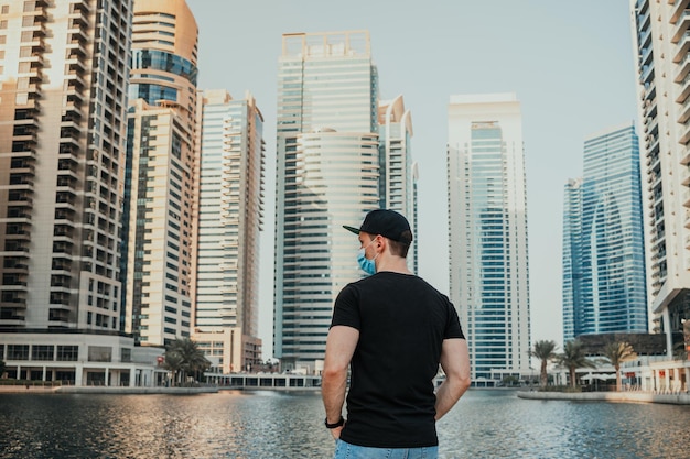 Young person tourist with medical mask standing outdoor and looking forward with urban background