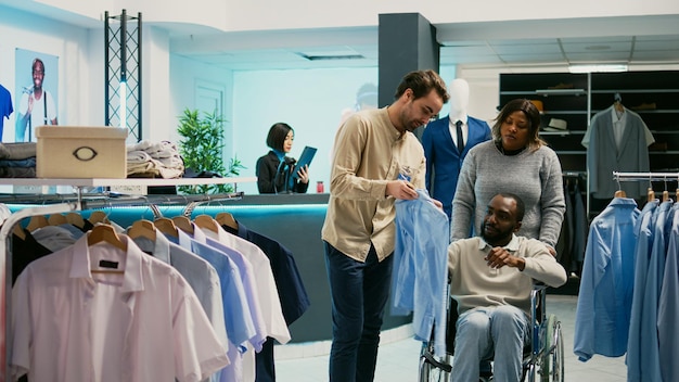 Young person with physical disability checking clothes in store, shopping for new collection brands in clothing shop. Wheelchair user buying formal wear from fashion boutique, commercial activity.