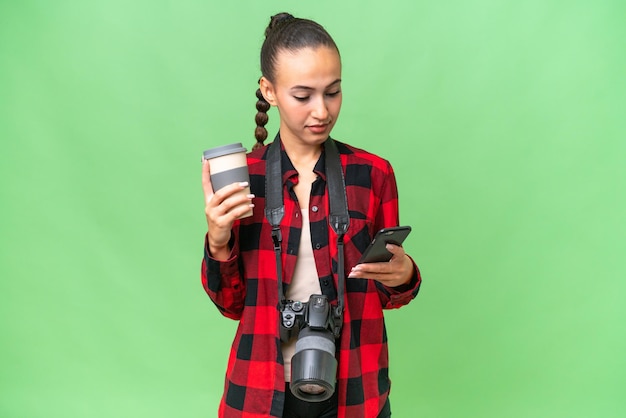 Young photographer Arab woman over isolated background holding coffee to take away and a mobile