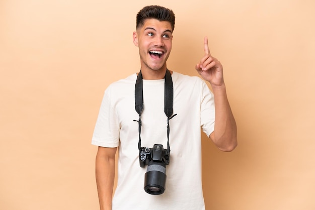 Young photographer caucasian man isolated on beige background intending to realizes the solution while lifting a finger up