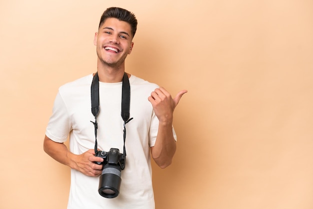 Young photographer caucasian man isolated on beige background pointing to the side to present a product