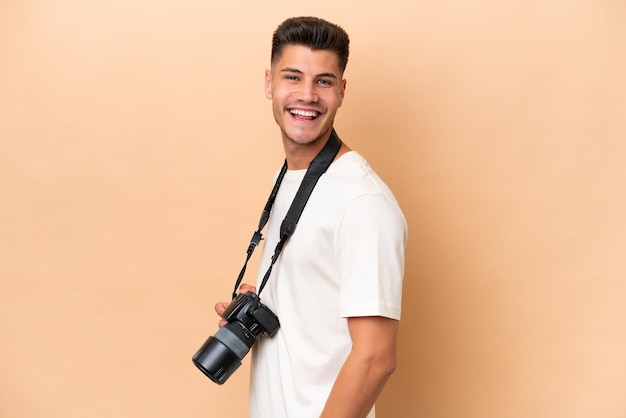 Young photographer caucasian man isolated on beige background with arms crossed and looking forward