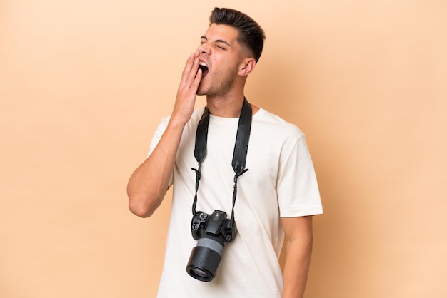 Young photographer caucasian man isolated on beige background yawning and covering wide open mouth with hand