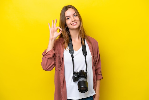 Young photographer caucasian woman isolated on yellow background showing ok sign with fingers