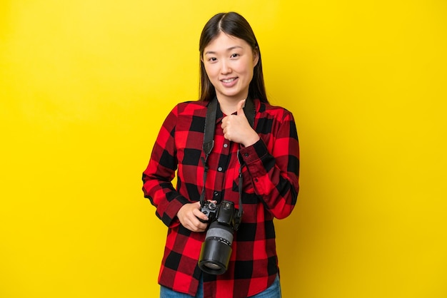 Young photographer Chinese woman isolated on yellow background giving a thumbs up gesture