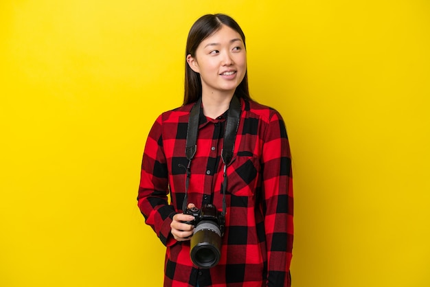 Young photographer Chinese woman isolated on yellow background happy and smiling