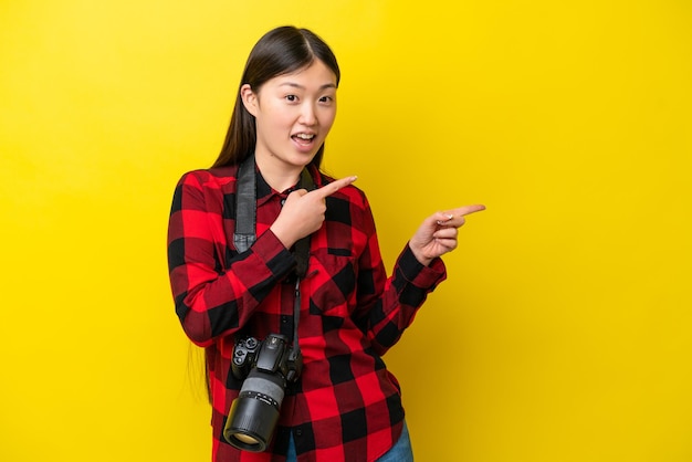 Young photographer Chinese woman isolated on yellow background surprised and pointing side