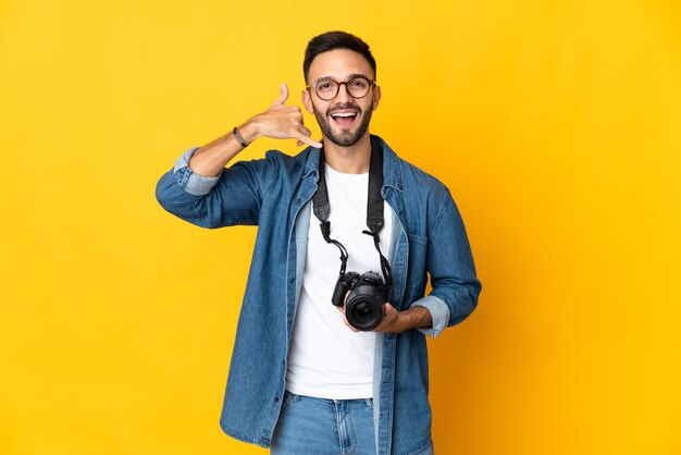 Young photographer girl isolated on yellow background making phone gesture. Call me back sign