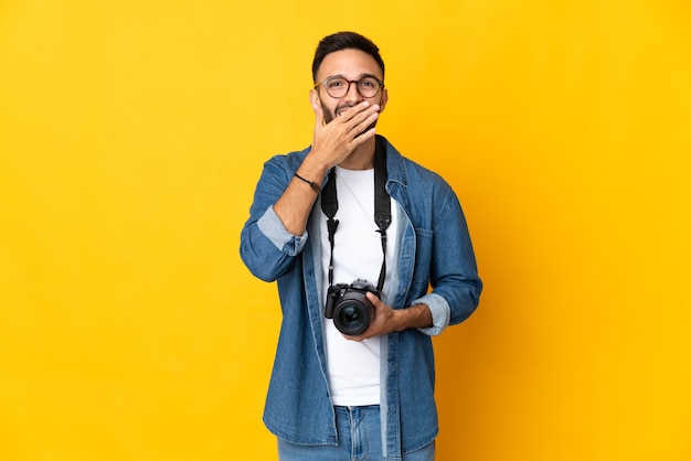 Young photographer girl isolated on yellow wall happy and smiling covering mouth with hand