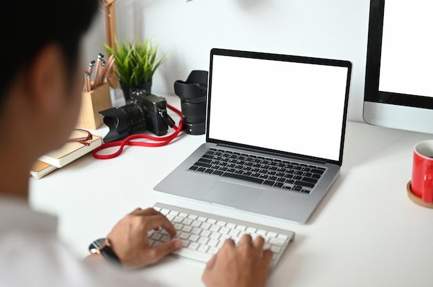 A young photographer is using a laptop with white screen on white desk