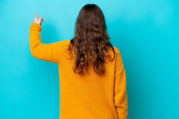 Young photographer woman isolated on blue background pointing back with the index finger