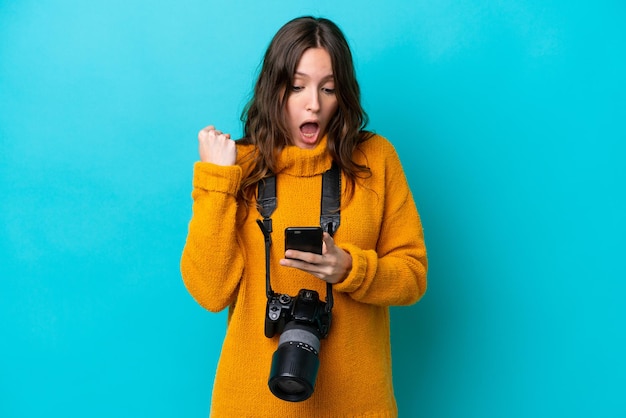 Young photographer woman isolated on blue background surprised and sending a message