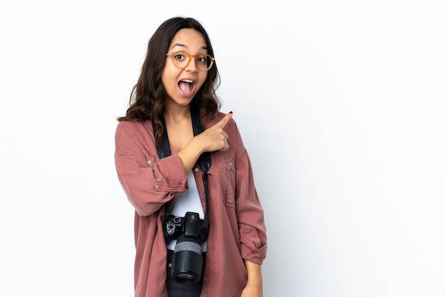 Young photographer woman over white wall surprised and pointing side