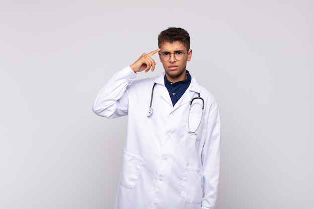 Young physician man feeling confused and puzzled, showing you are insane, crazy or out of your mind