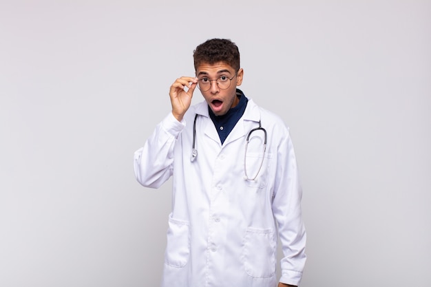 Young physician man looking surprised, open-mouthed, shocked, realizing a new thought, idea or concept