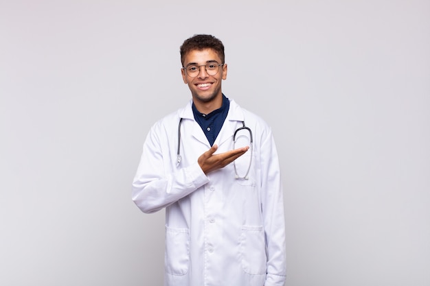 young physician man smiling cheerfully, feeling happy and showing a concept in copy space with palm of hand