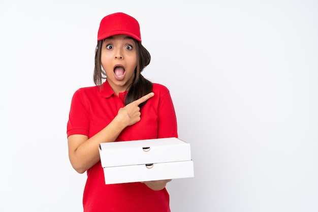 Young Pizza delivery girl over isolated white wall surprised and pointing side