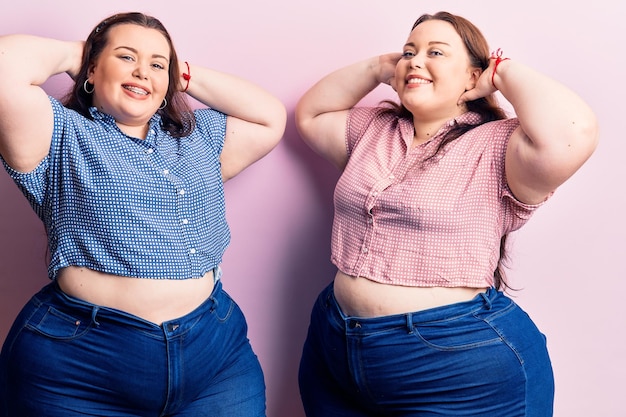 Young plus size twins wearing casual clothes relaxing and stretching, arms and hands behind head and neck smiling happy