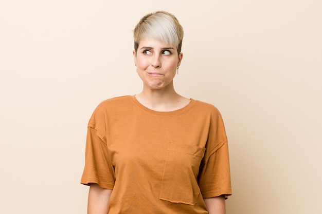 Young plus size woman with short hair confused, feels doubtful and unsure.