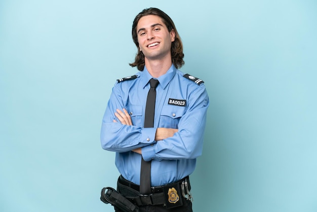 Young police caucasian man isolated on blue background with arms crossed and looking forward