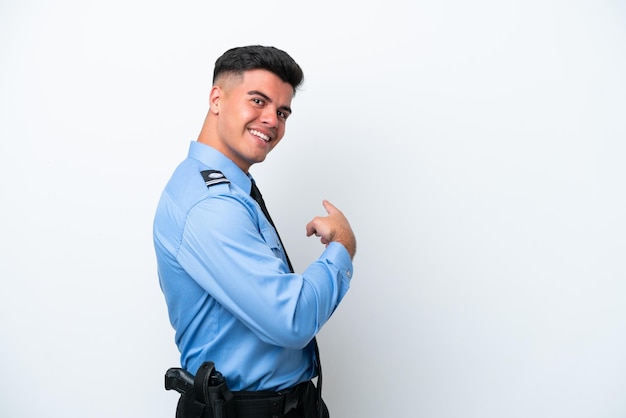 Young police caucasian man isolated on white background pointing back