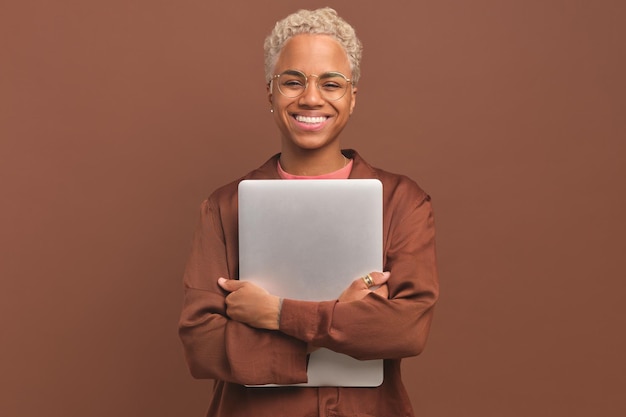 Young positive african american woman clutching laptop to chest stands in studio