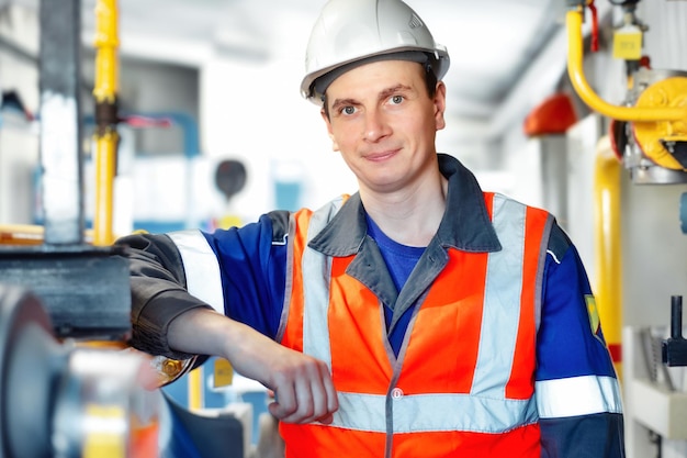 Young positive engineer in helmet and construction vest looks into camera and smiles Portrait Gas industry worker