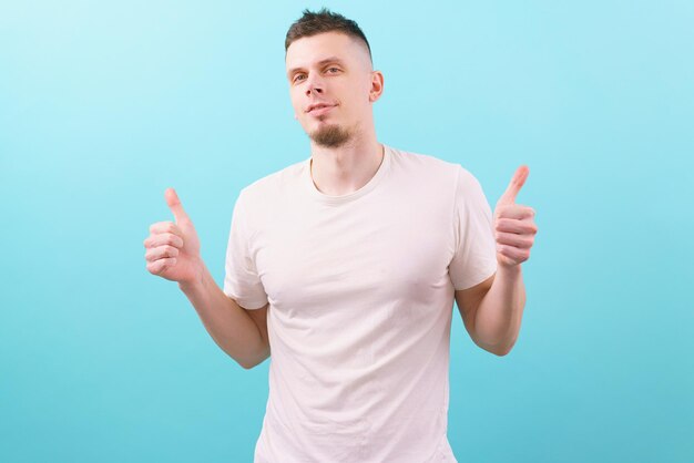 young positive man wearing a white t-shirt shows his fingers thumbs up on a blue Portrait Attractive