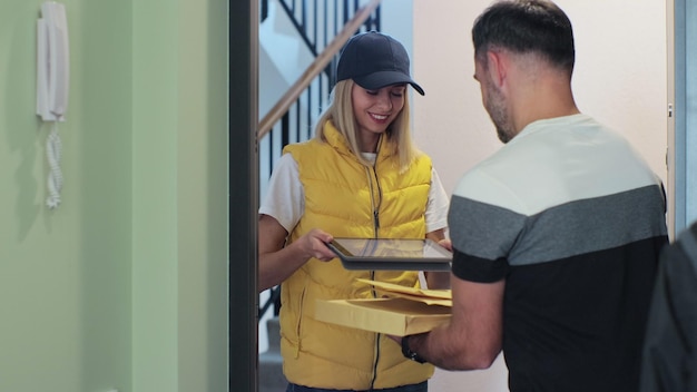 Young postwoman delivering parcel to the customer asking him to sign up a document in digital tablet Post delivery modern services