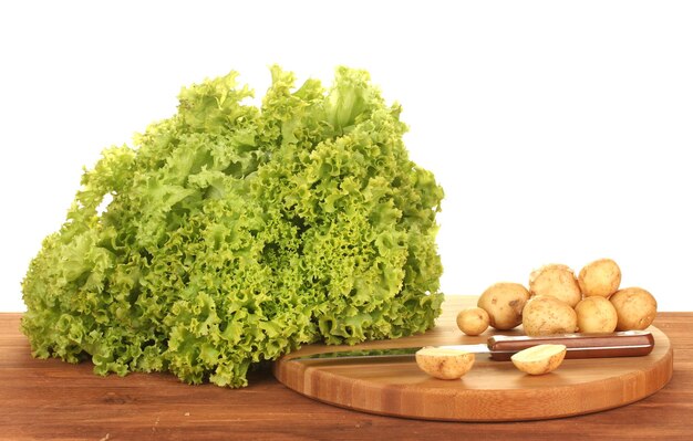 Young potatoes and lettuce on a cutting board with knife on a table on white background closeup