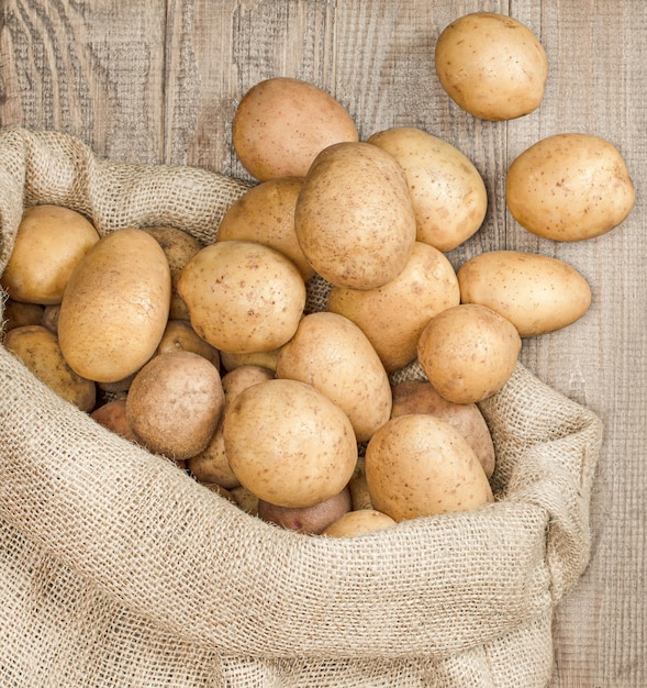 Young potatoes scattered from a bag on a wooden table, top view