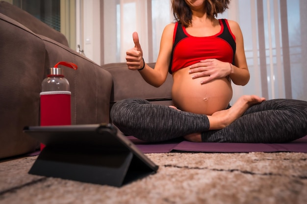 Young pregnant caucasian brunette giving thumbs up to online yoga teacher Online exercises in prepartum classes wellness during pregnancy