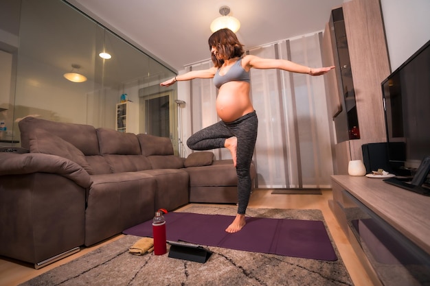 A young pregnant Caucasian woman doing pilates exercise at home in the living room Online exercises in prepartum classes