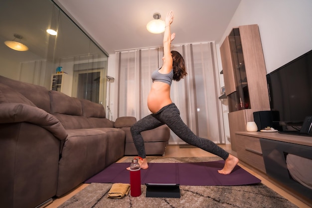 Young pregnant caucasian woman doing pilates exercise at home in the room Online exercises in prepartum classes