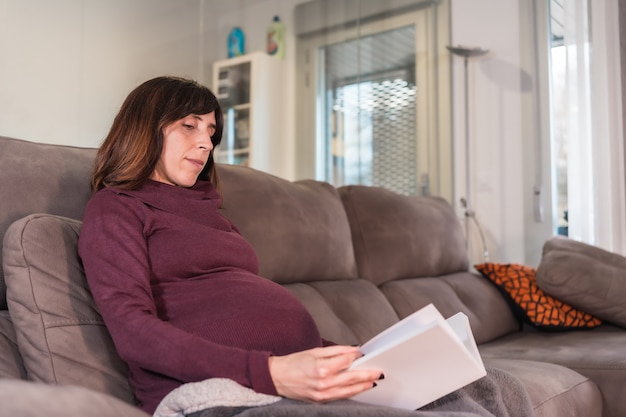 Young pregnant Caucasian woman enjoying the well-being of her home reading a book