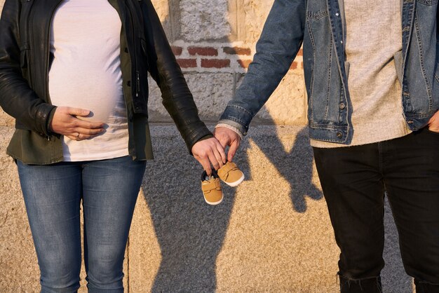 Young pregnant couple holding baby shoes. Family concept. Expecting newborn. Holding hands.